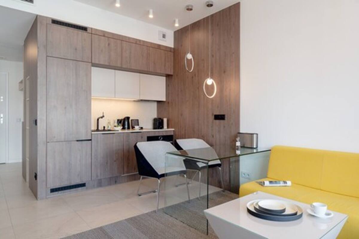 A modern kitchen with wooden cabinets, a glass dining table, and a yellow sofa.