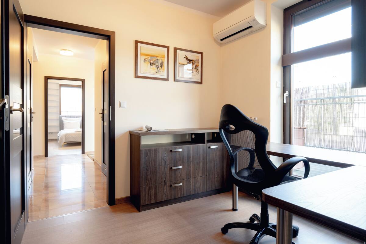 A modern hotel room with a wooden floor, a desk with a chair, a wardrobe, and two framed pictures on the wall.