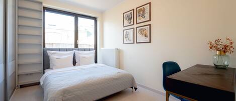 A bedroom with a bed, a bedside table, a chair, and a window.