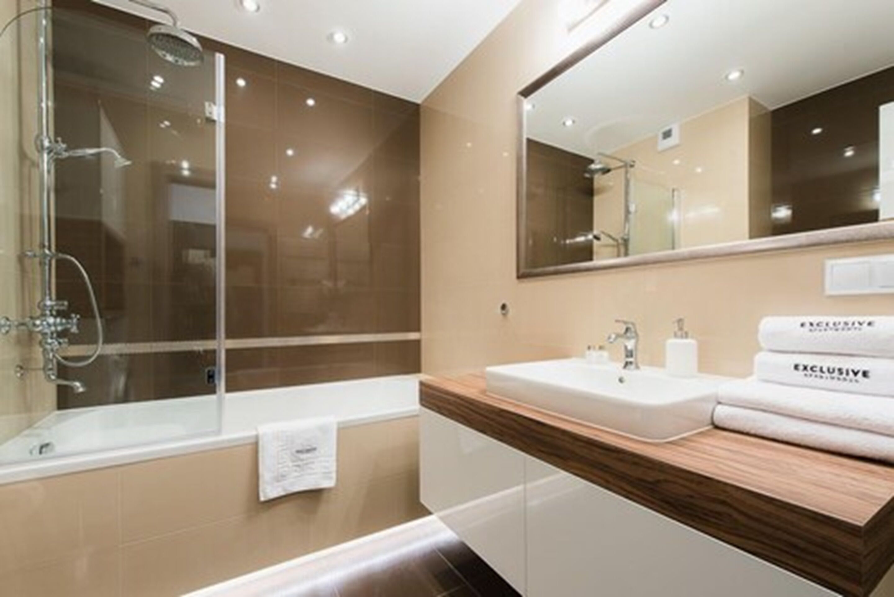 A modern bathroom with a glass shower enclosure, a large mirror, and a wooden vanity with a sink and towel rack.
