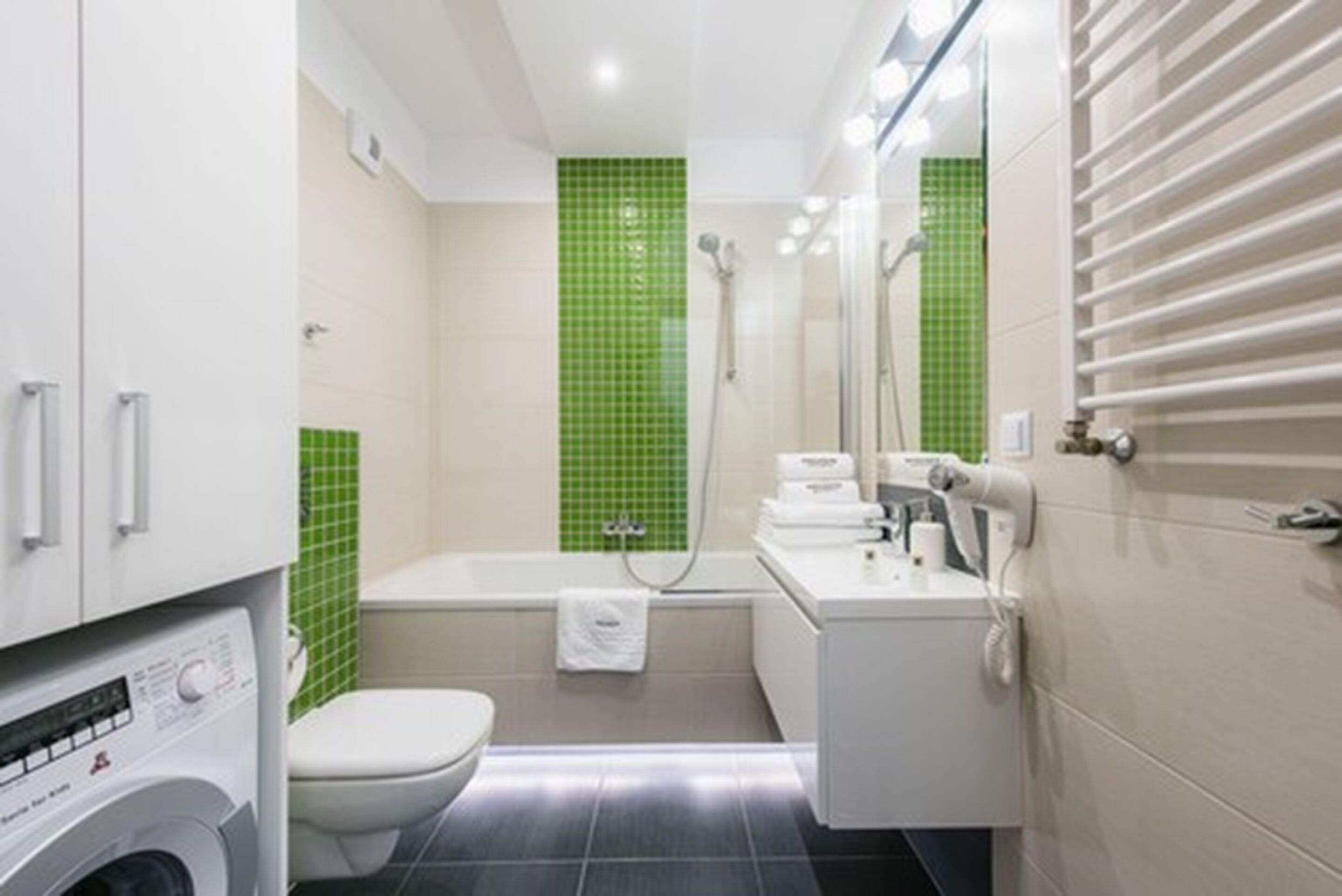 A compact bathroom with a toilet, a washing machine, a shower, and a sink.