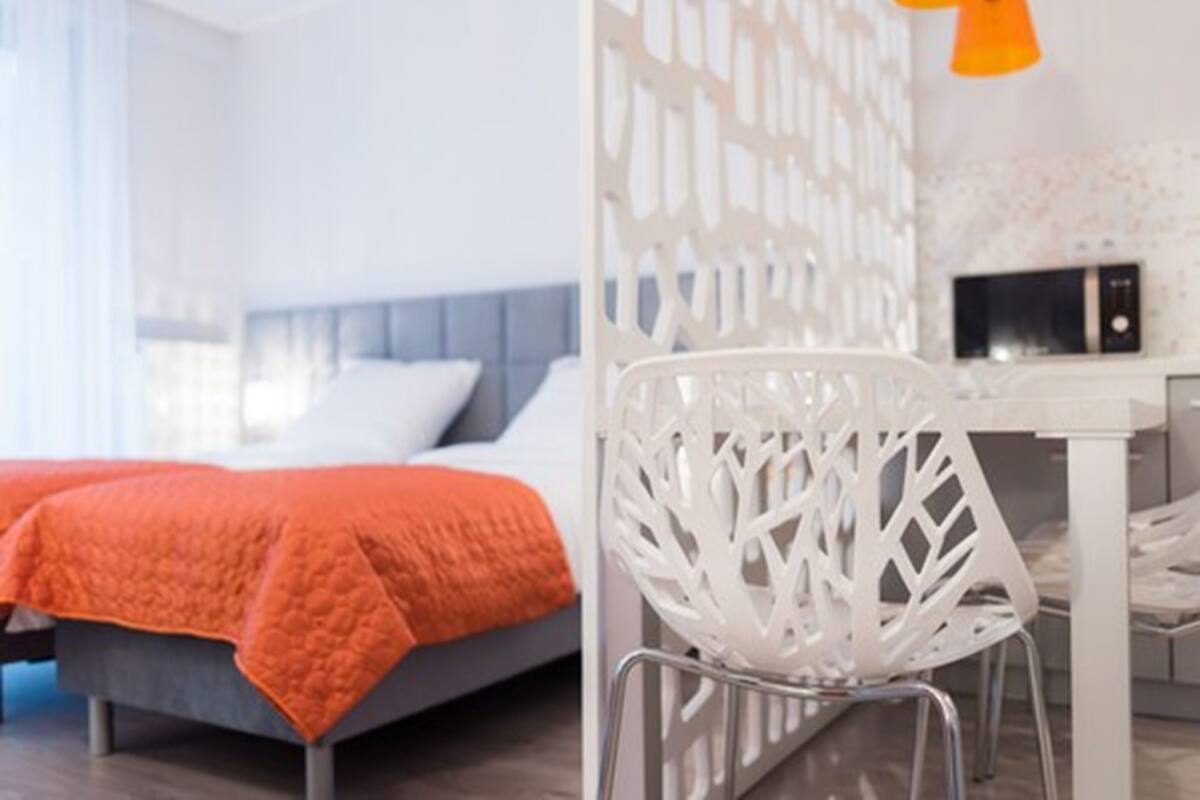 A modern bedroom with a bed, a white chair, and a desk with a computer.
