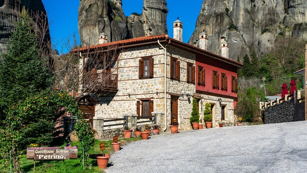 A stone building with a red facade, a balcony, and potted plants in front. - Guesthouse Sotiriou (Kalabaka)
