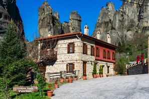 A stone building with a red facade, a balcony, and potted plants in front. - Guesthouse Sotiriou (Kalabaka)