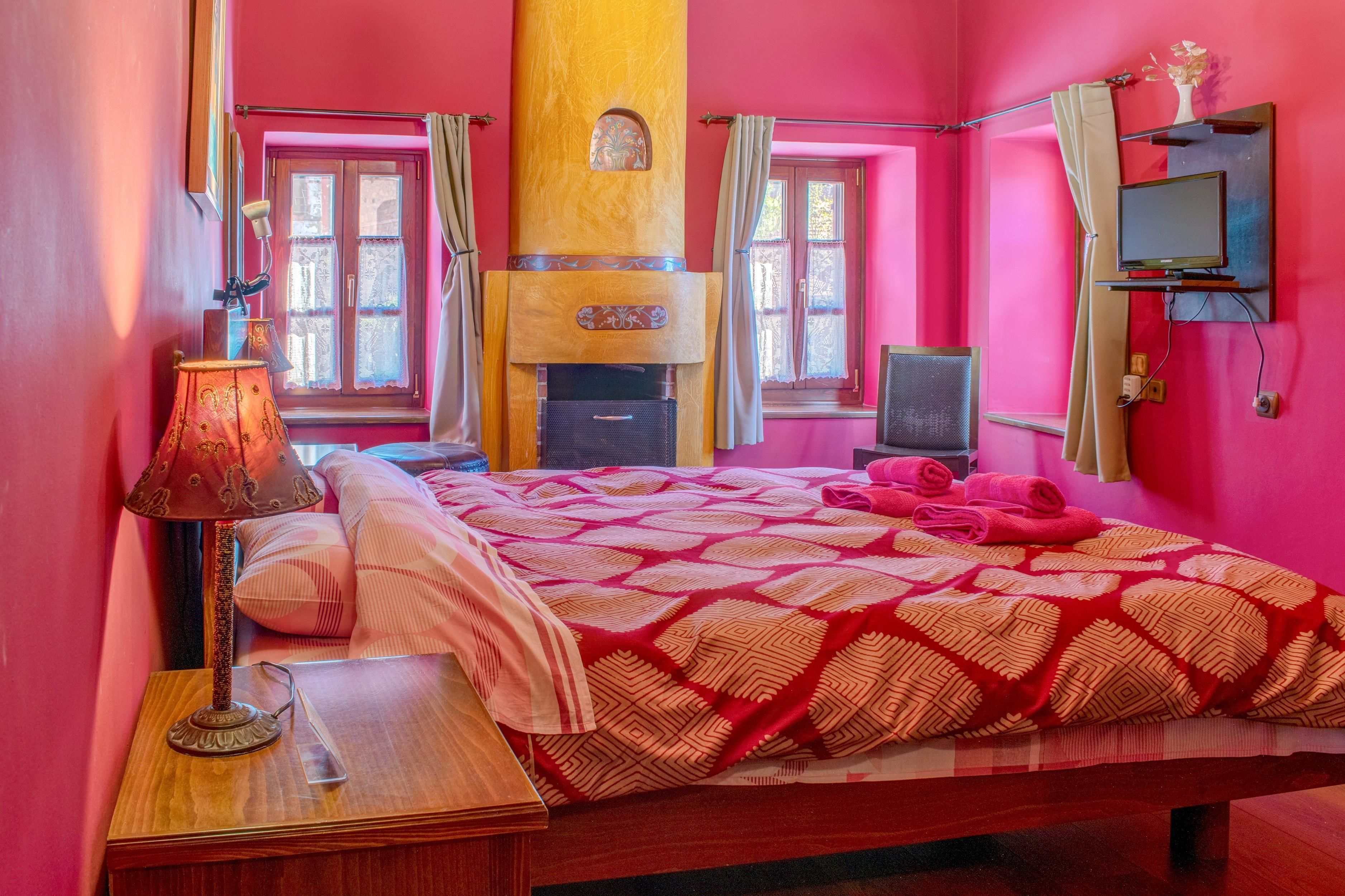 A room with a bed, a lamp, a television, and a window with curtains.