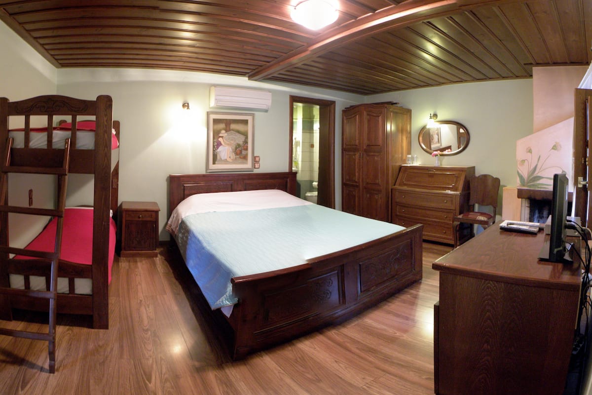 A bedroom with a wooden bunk bed, a large wooden bed, a dresser, and a desk with a mirror.