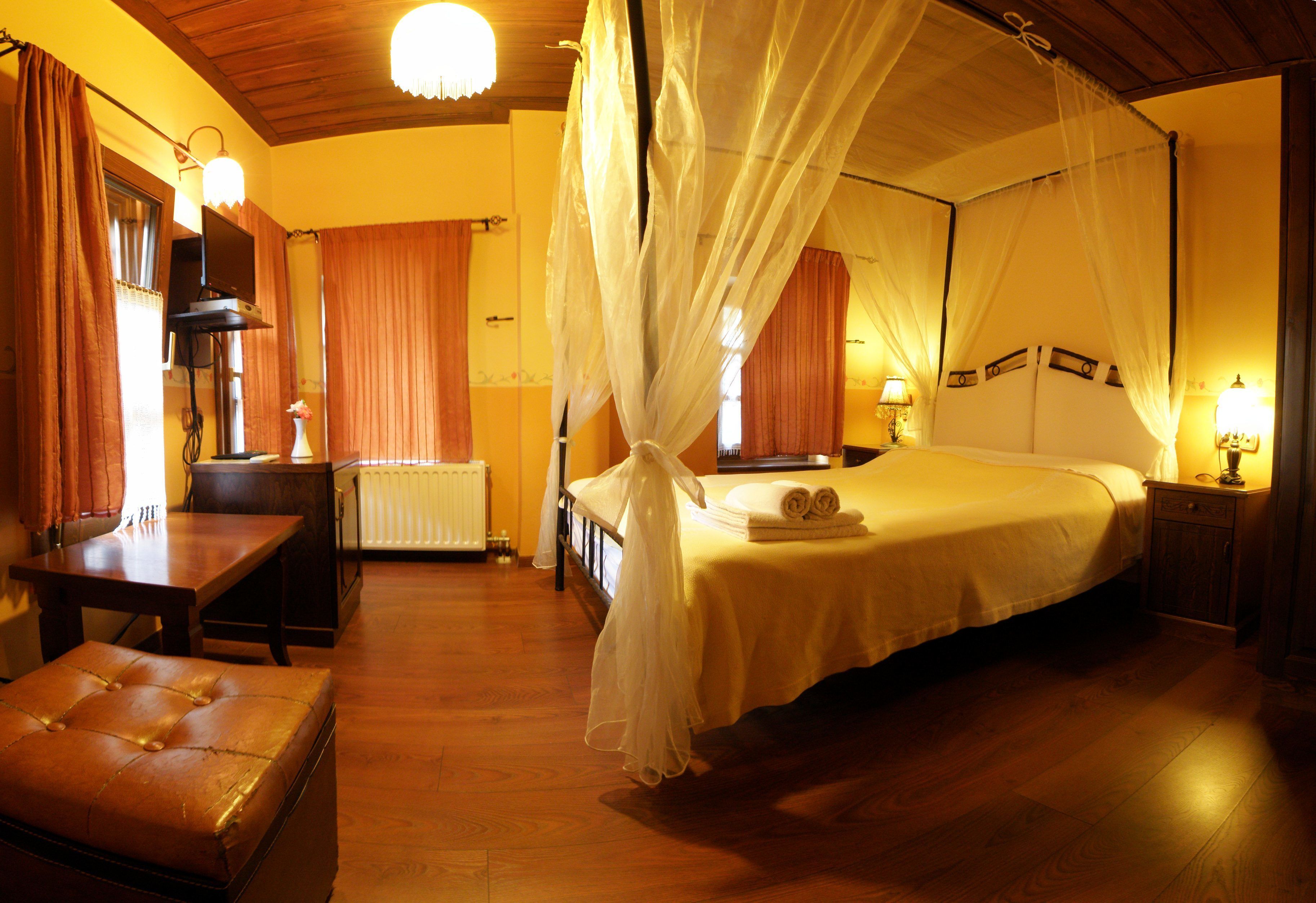 A bedroom with a canopy bed, wooden flooring, a desk, and a radiator.