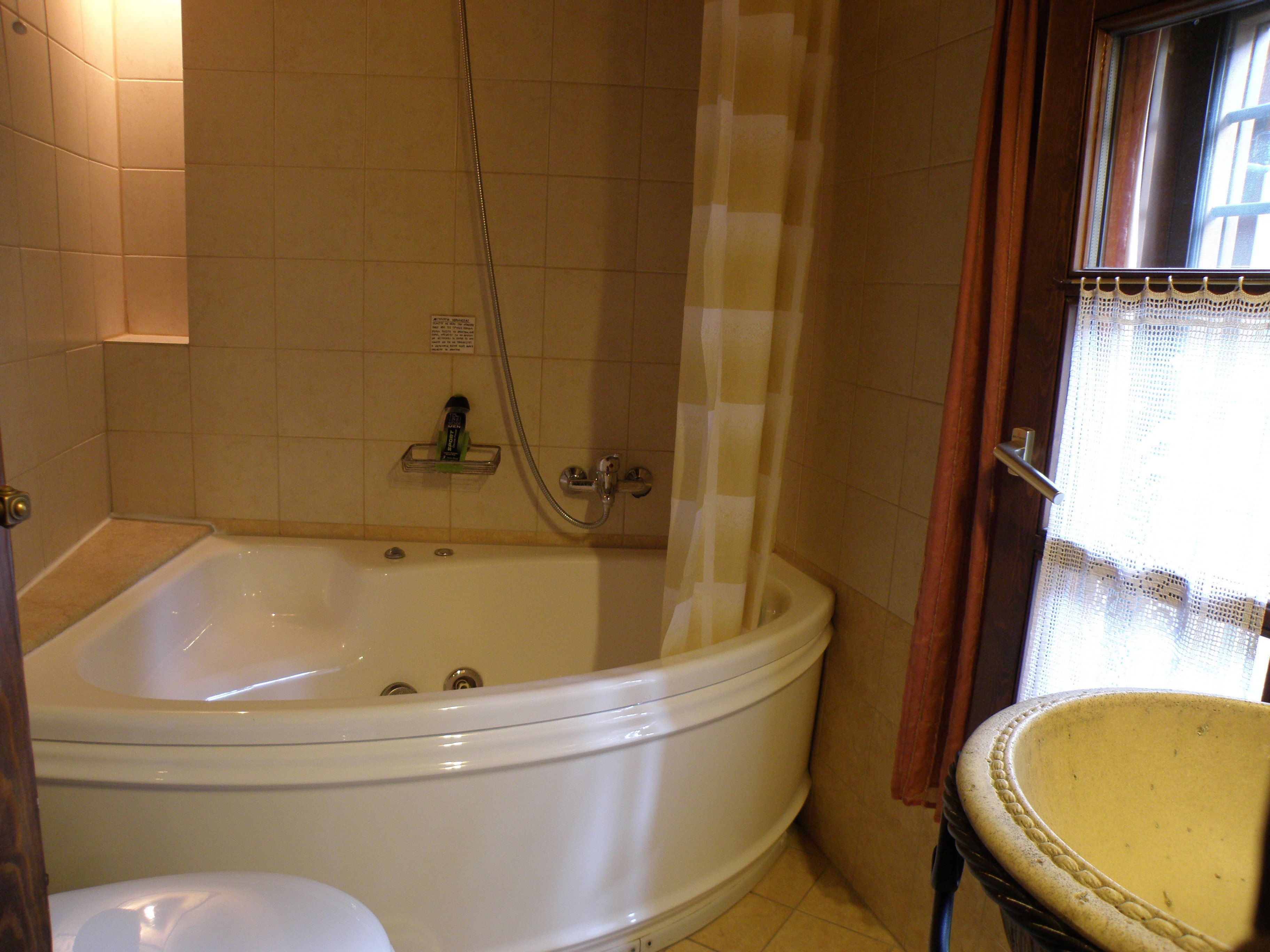 Un baño con bañera, inodoro y ventana con cortina.