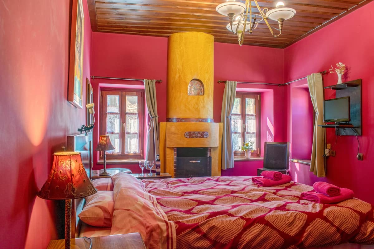 A room with a large bed, a fireplace, a television, and a window with curtains.