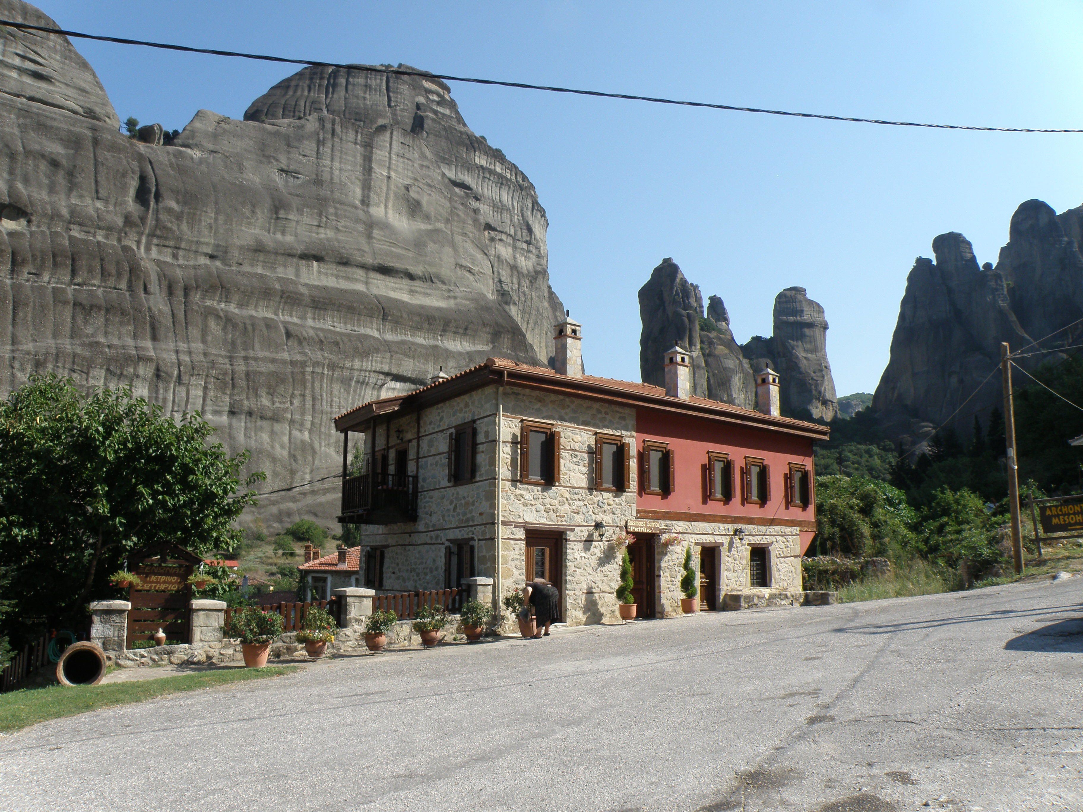 A stone building with a red facade, surrounded by potted plants and a road leading to a mountainous area.