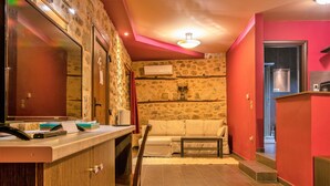 A room with a stone wall, a wooden counter, a sofa, and a red wall. - Guesthouse Sotiriou (Kalabaka)
