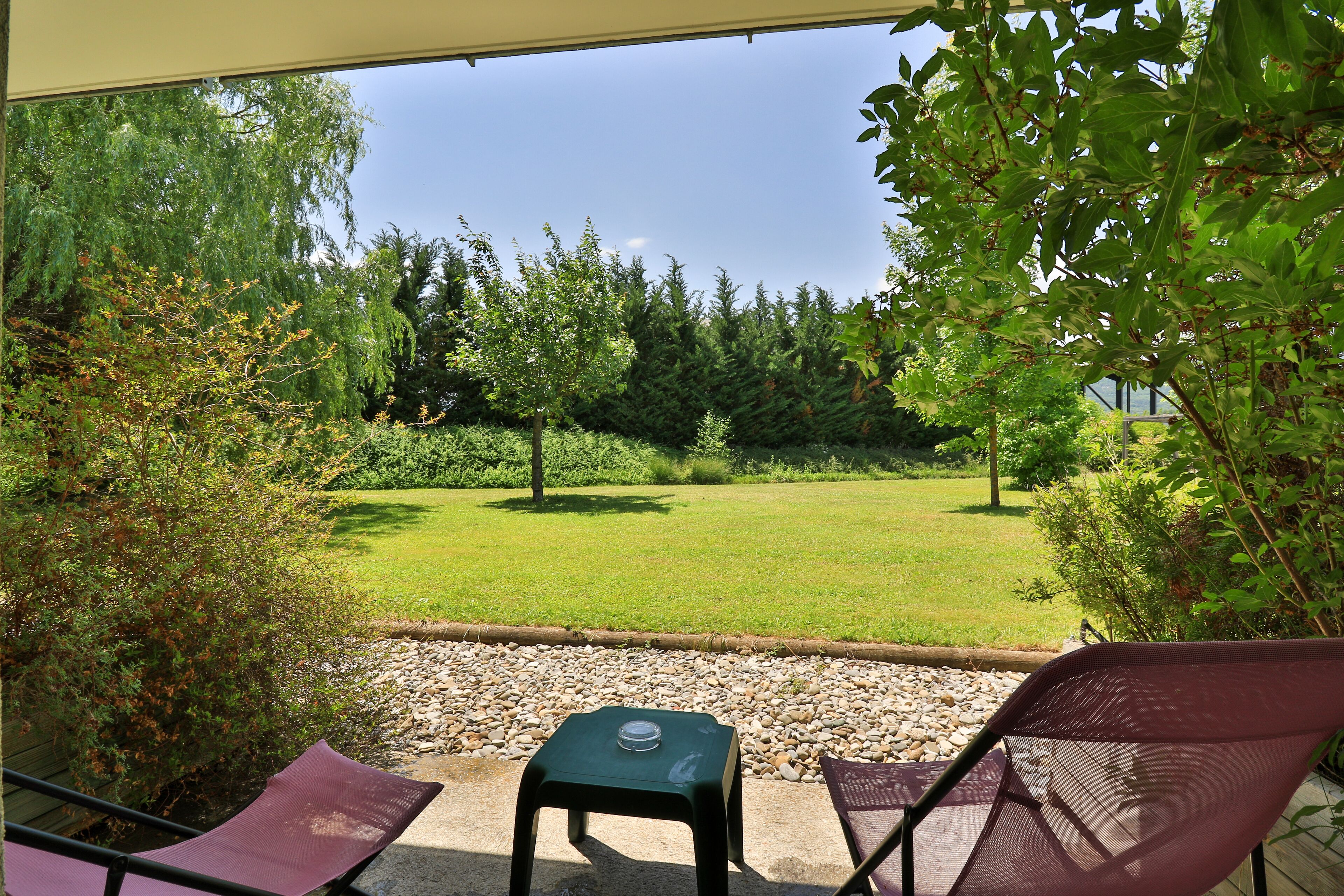 A patio with two chairs and a table, overlooking a grassy area with trees and a clear sky.