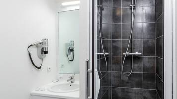 Ein modernes Badezimmer mit einer gläsernen Duschkabine, einem weißen Waschbecken und einem Spiegel darüber.