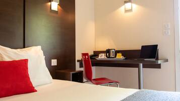 A hotel room with a bed, a desk with a laptop, a red chair, and two wall-mounted lights.