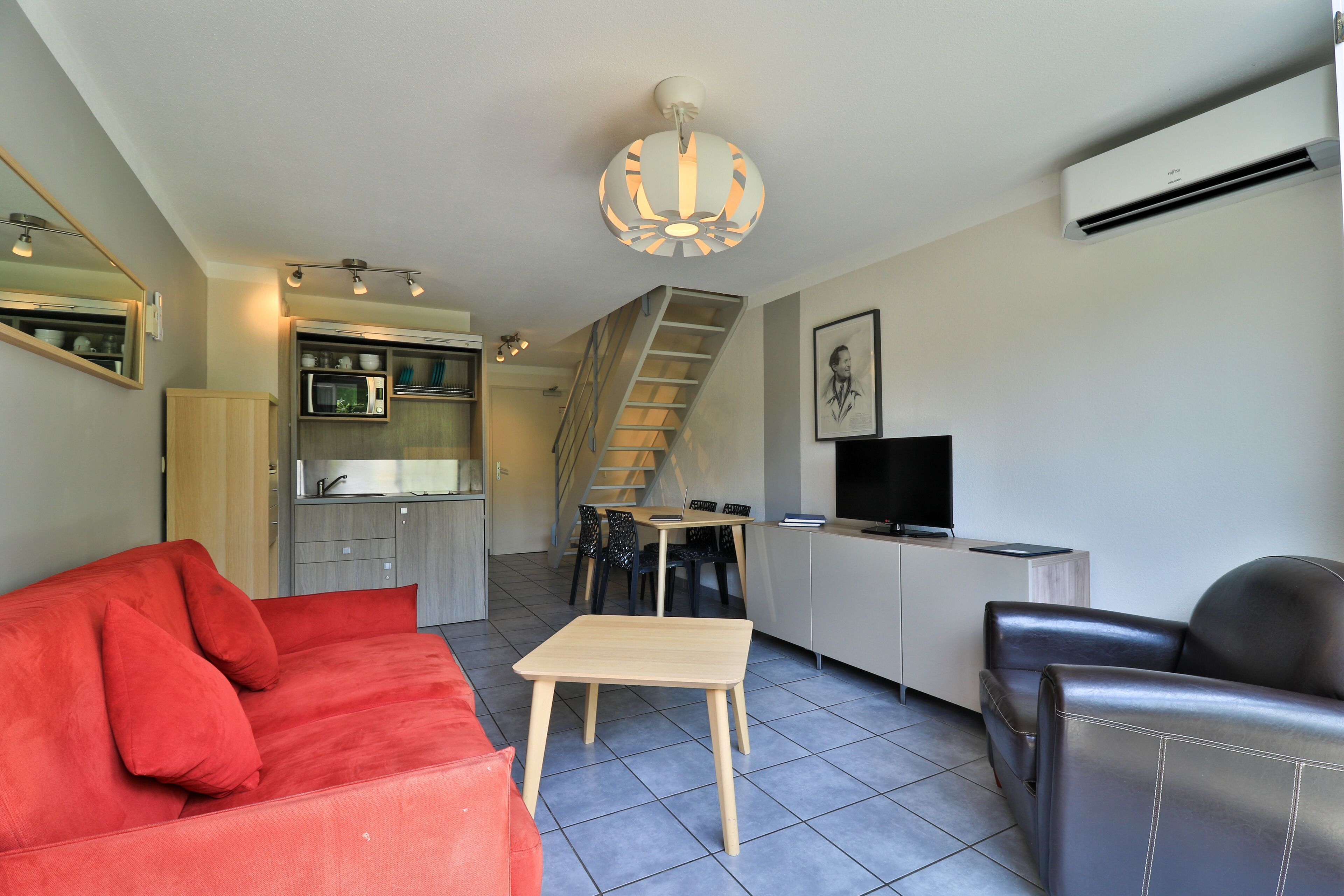 A compact living space with a sofa, a dining table, a TV, and a staircase leading to an upper level.