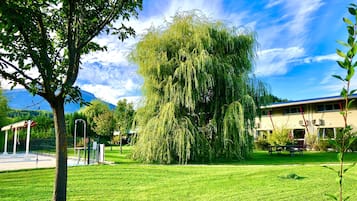 A grassy area with a large weeping willow tree, a building with a blue roof, and a clear sky.