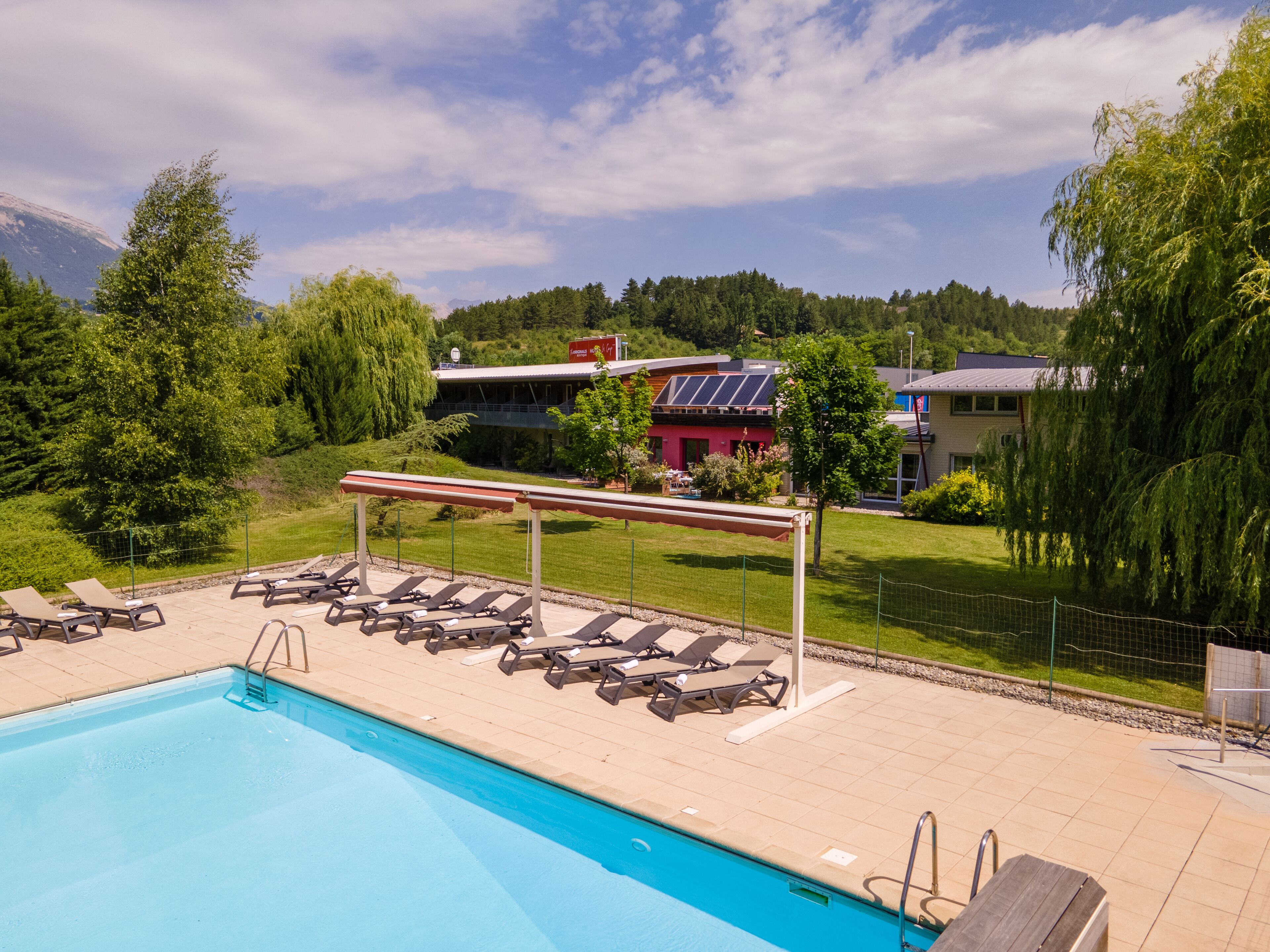 A swimming pool with sun loungers and a view of buildings and trees in the background.