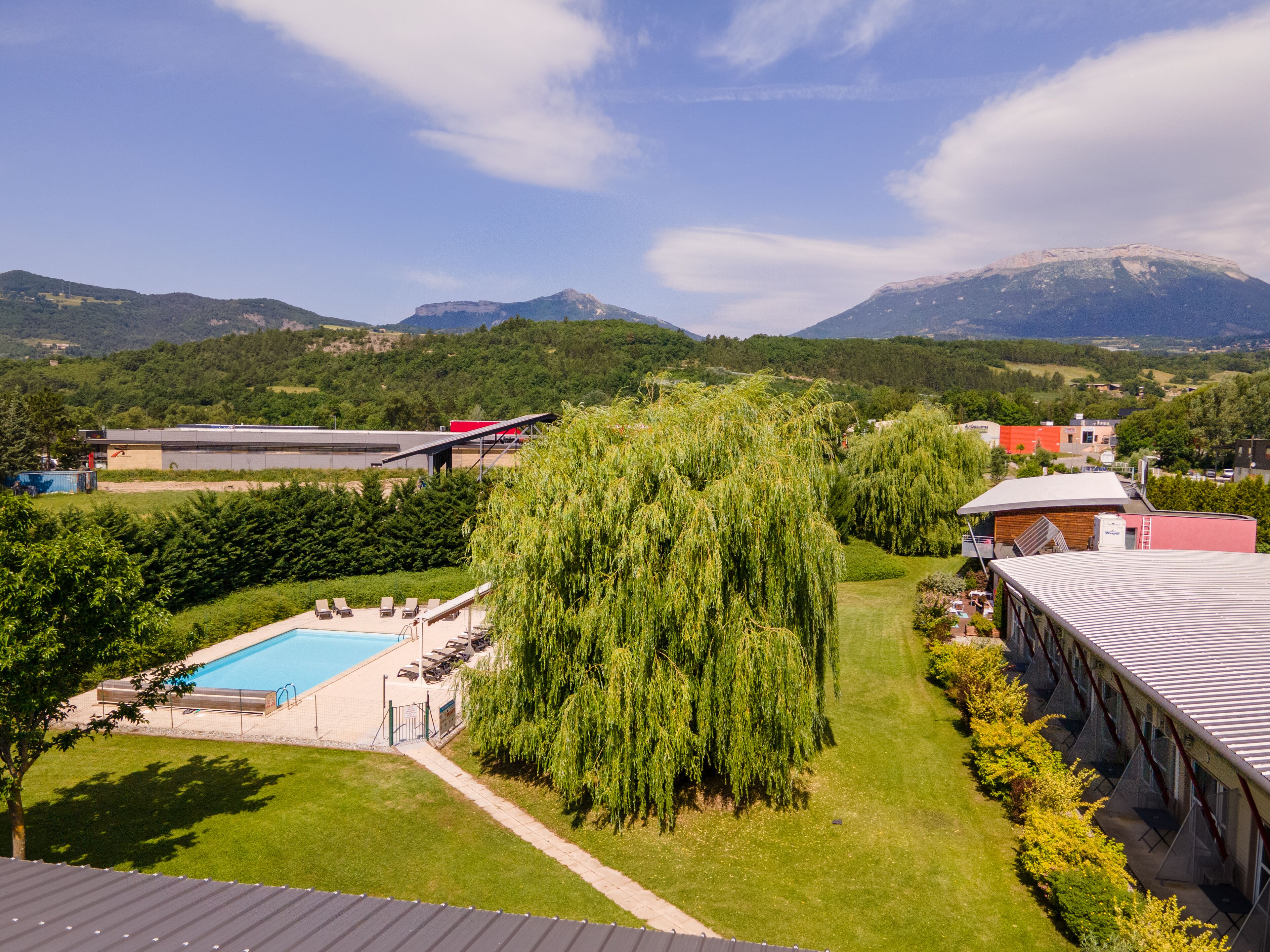A hotel with a swimming pool, lush greenery, and mountains in the background.