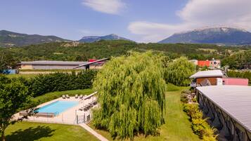 A hotel with a swimming pool, lush greenery, and mountains in the background.