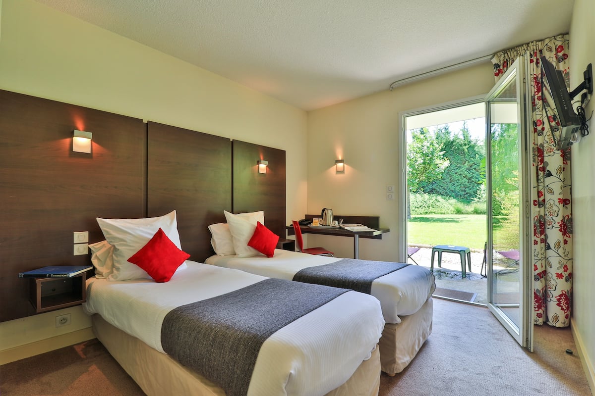 Una habitación de hotel con dos camas, un escritorio y vistas a un jardín.