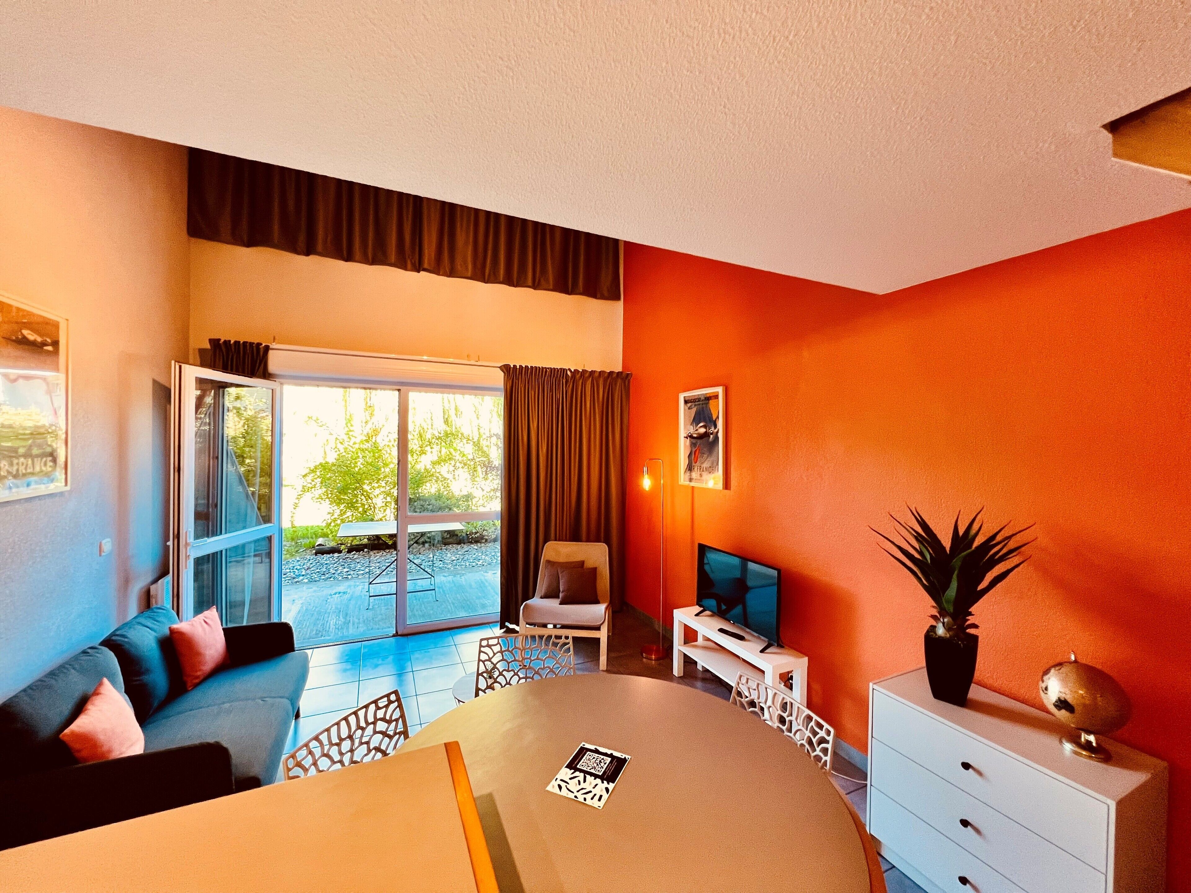 Una sala moderna con sofá, mesa de comedor y televisor. Cuenta con una puerta corrediza de vidrio que da a un espacio exterior.