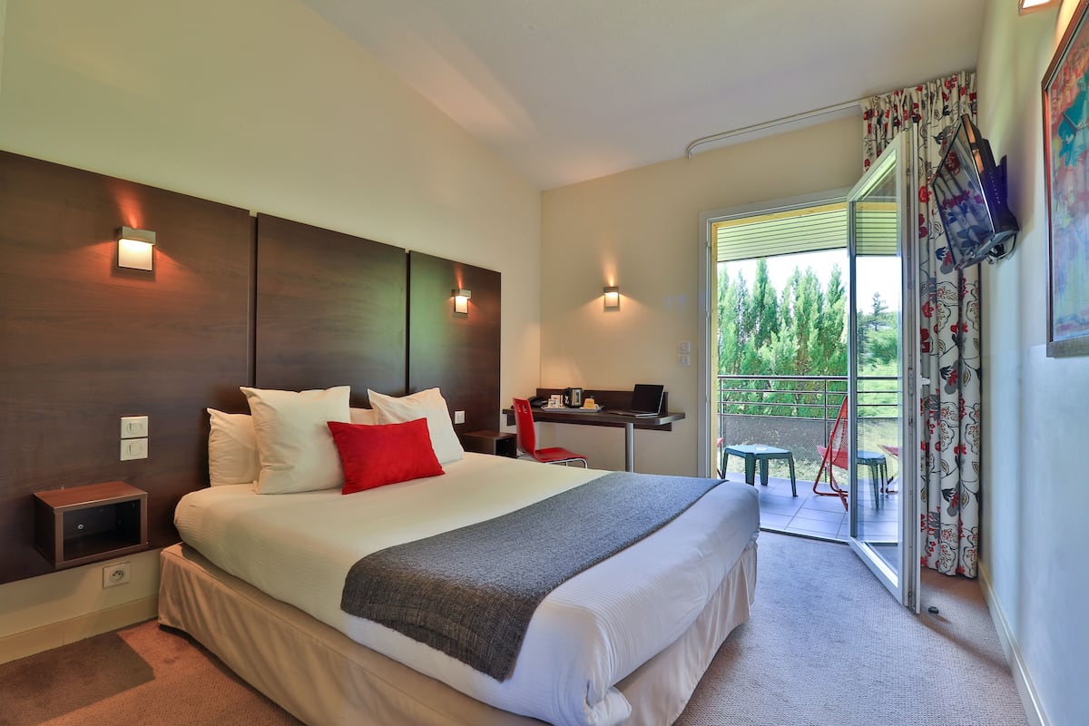 Una habitación de hotel moderna con una cama grande, un escritorio y un balcón con mobiliario exterior.