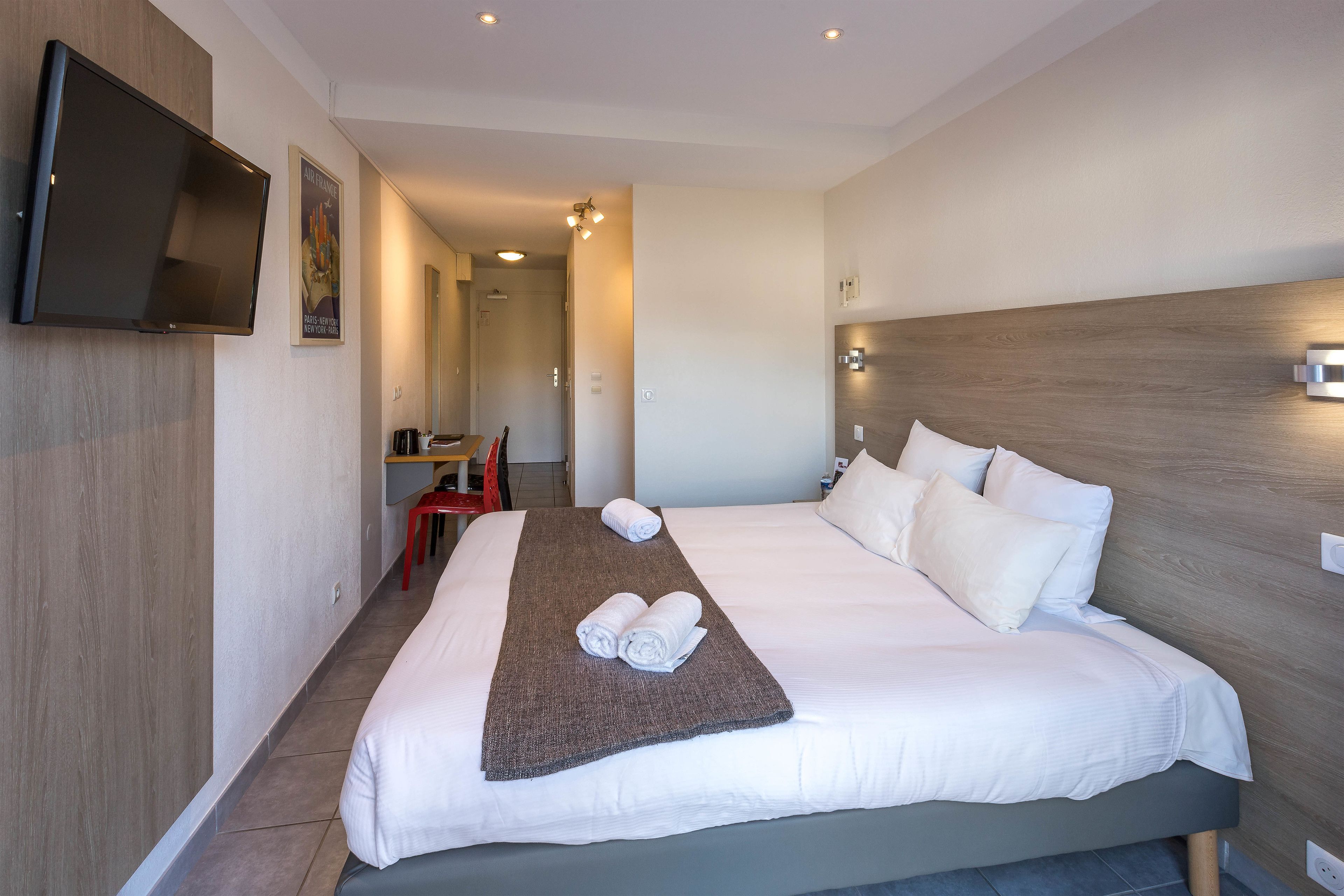 A hotel room with a large bed, a flat-screen TV mounted on the wall, and a wooden headboard.