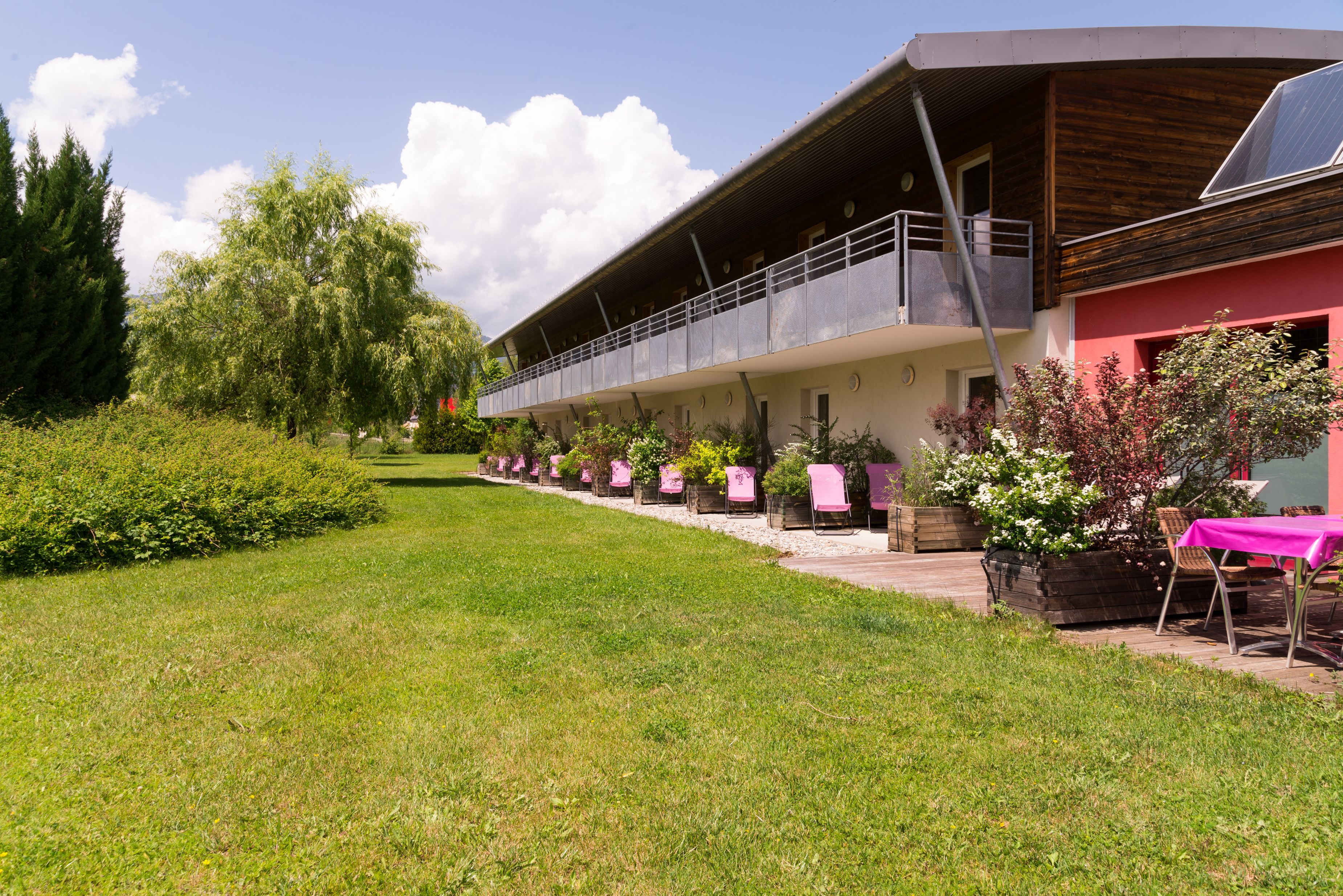 Un bâtiment doté d’un espace extérieur abrité, d’une pelouse et de plantes en pot.