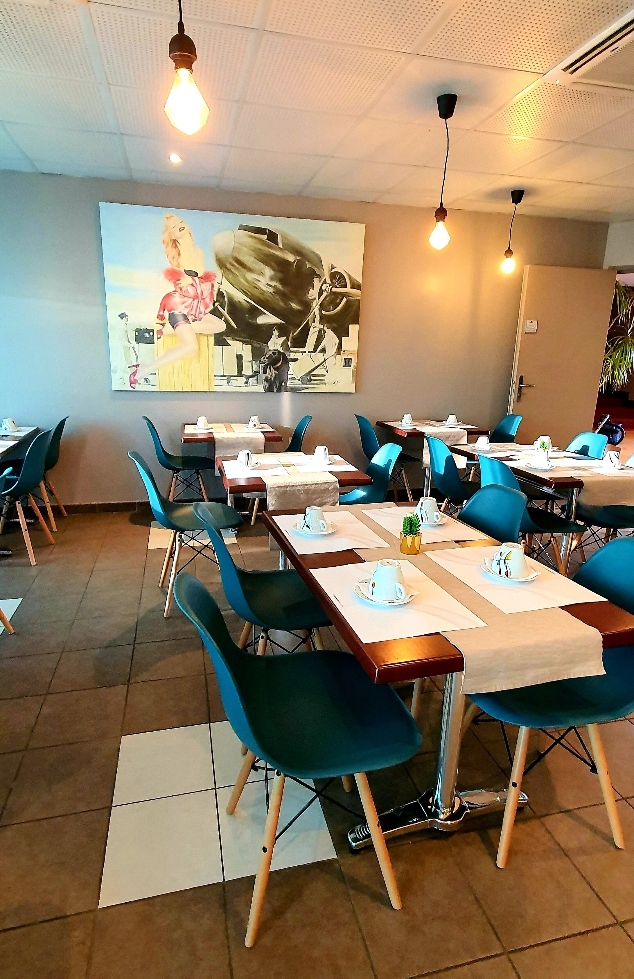 A dining area with tables set for service, blue chairs, and hanging light fixtures.