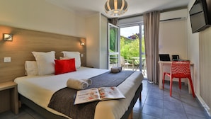 Ein Hotelzimmer mit Bett, Schreibtisch, Stuhl, Fernseher und einem Balkon mit Blick auf Grünflächen.