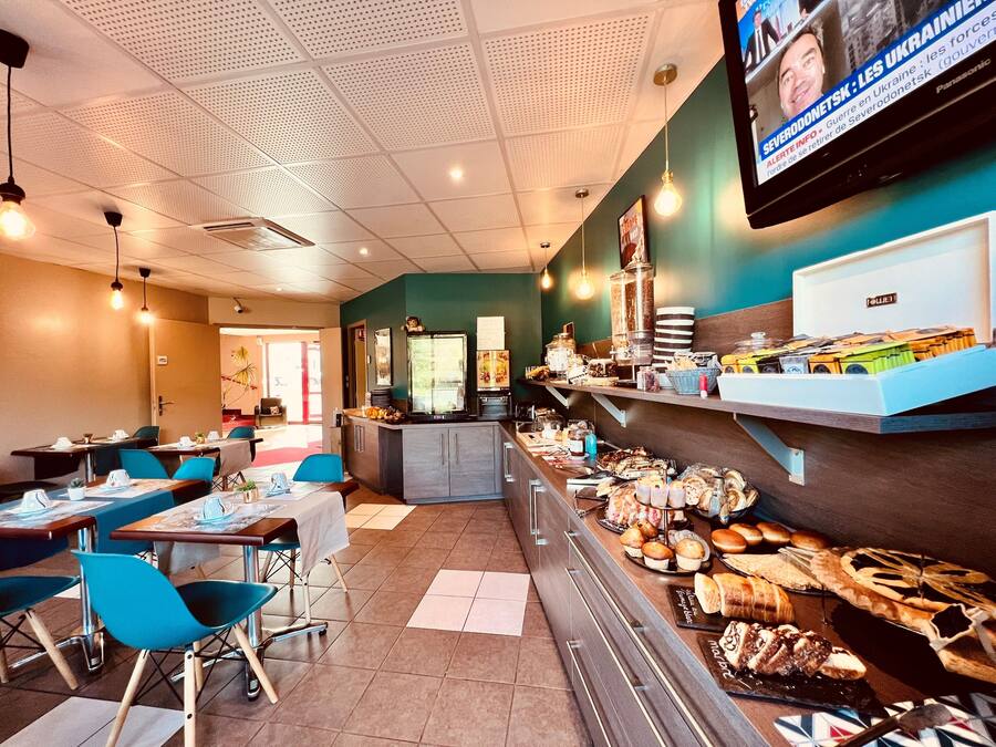 A restaurant with tables and chairs, a counter with food items, and a television screen displaying news.