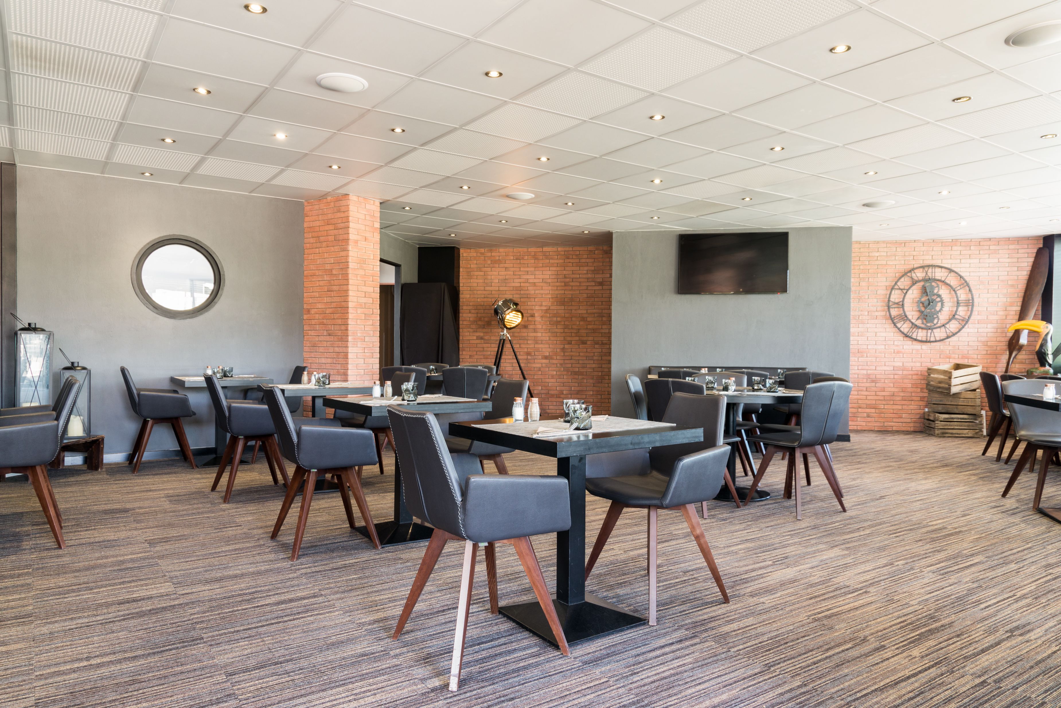 A modern dining area with round tables, black chairs, and a brick accent wall.