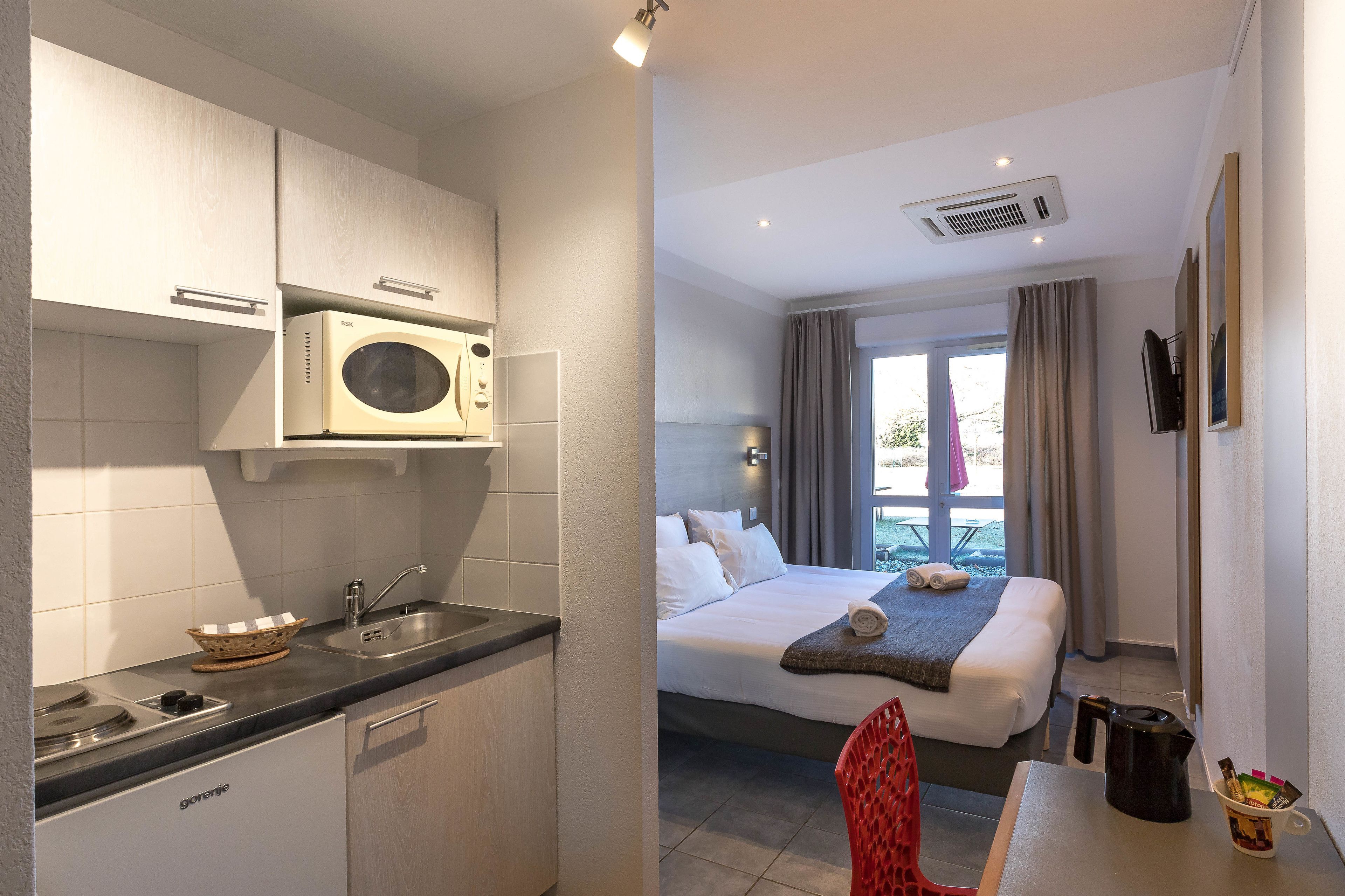 Una habitación de hotel compacta con kitchenette, cama con vistas y zona de comedor.
