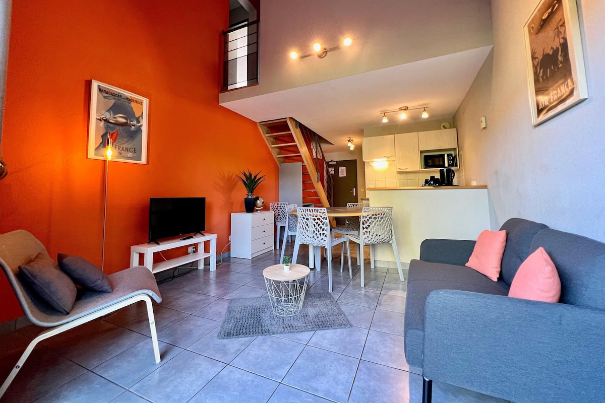 Un espacio habitable compacto con comedor, kitchenette y televisión en la sala.