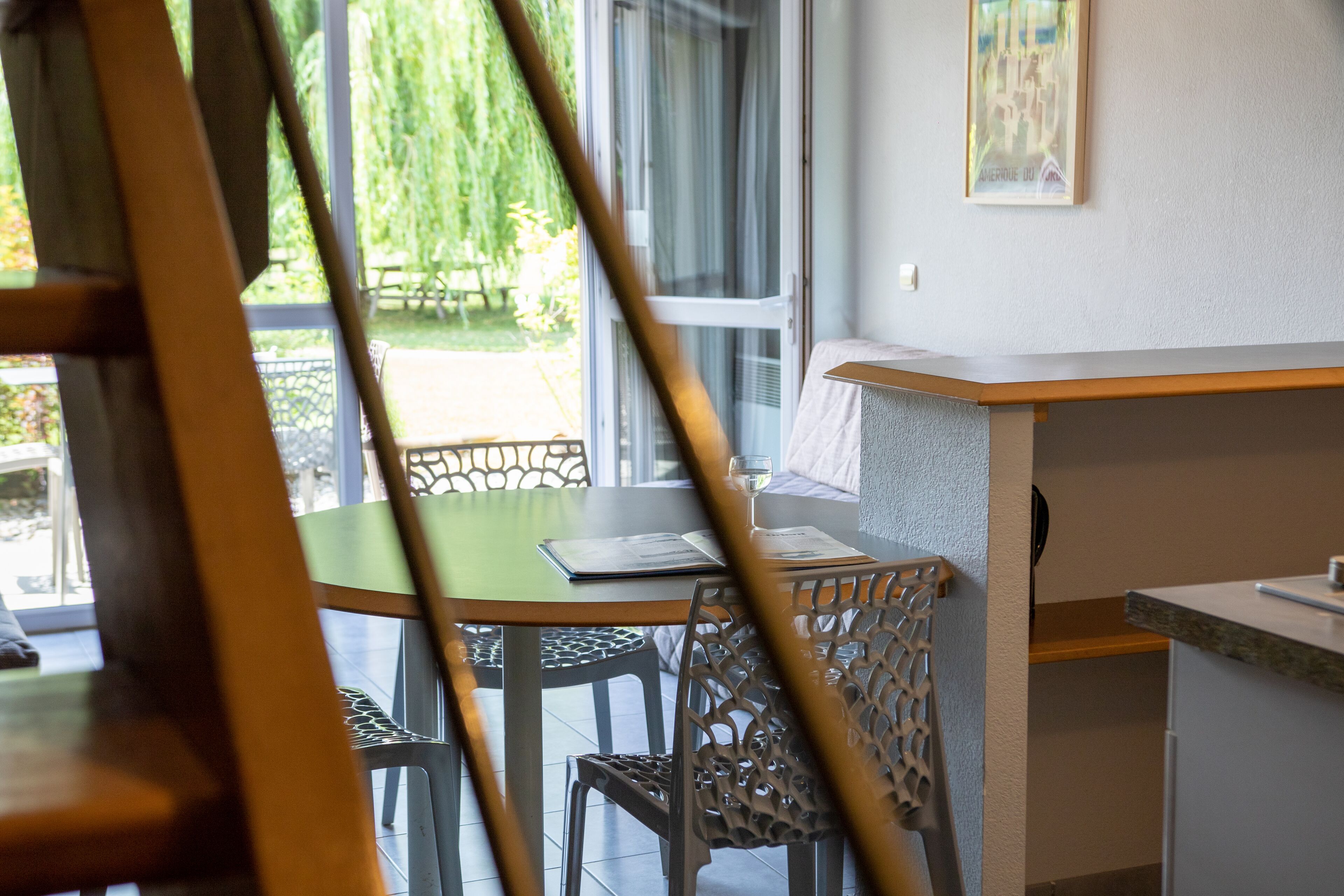 A dining area with a table and chairs, a window with a view of greenery, and a counter with a towel.