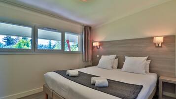 A hotel room with a large bed, two bedside tables, a window with blinds, and a wall-mounted lamp.