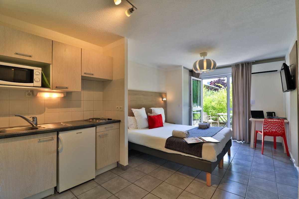 Habitación de hotel compacta con kitchenette, una cama con almohadas, un escritorio con silla y vistas a zonas verdes.