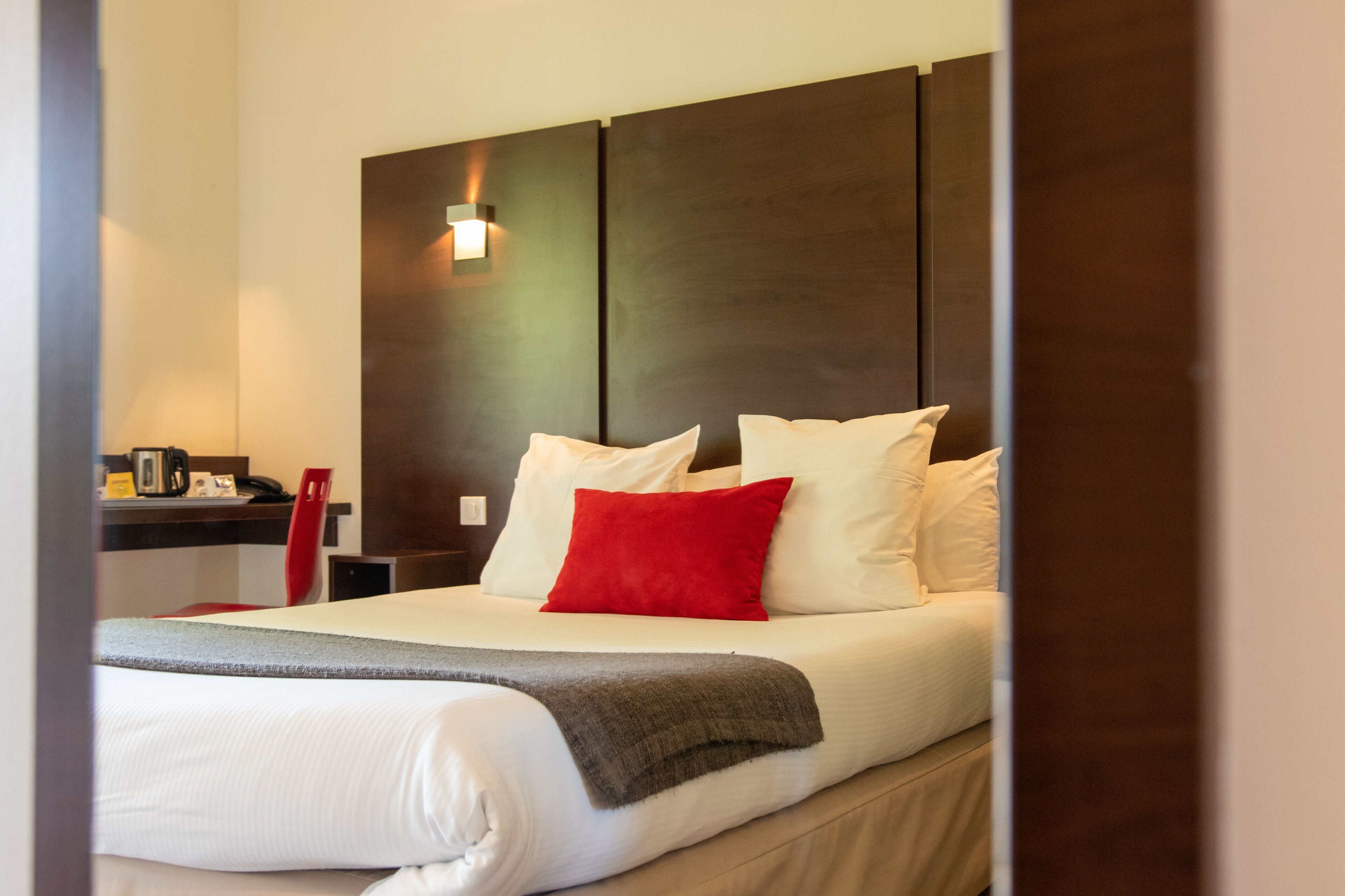 A hotel room with a bed, a bedside table, a lamp, and a wall-mounted light fixture.