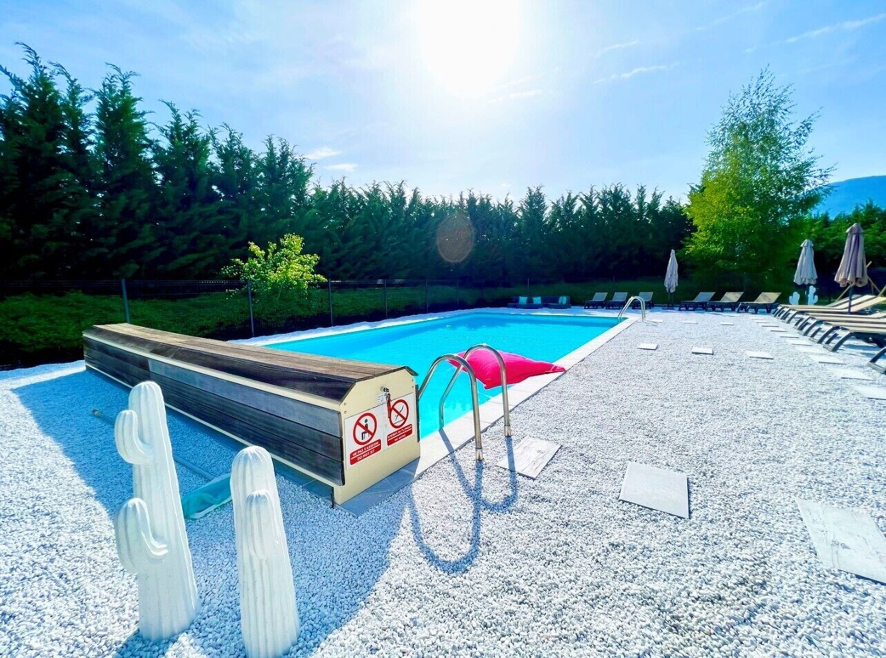 A swimming pool with a wooden deck, a red lounge chair, and a lifeguard stand with a no swimming sign.