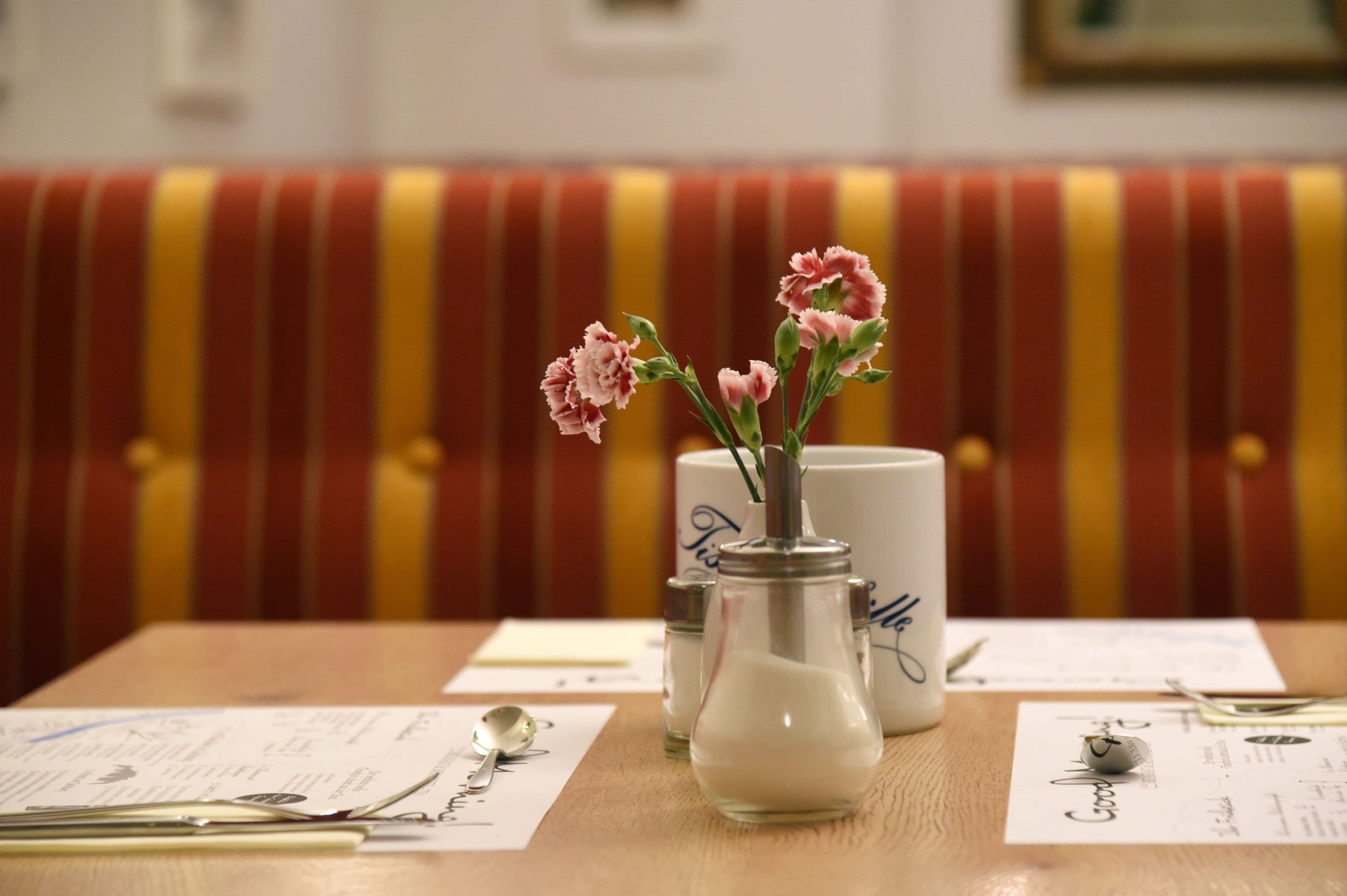 Una mesa con un florero, una taza blanca, saleros y pimenteros, y una cuchara.