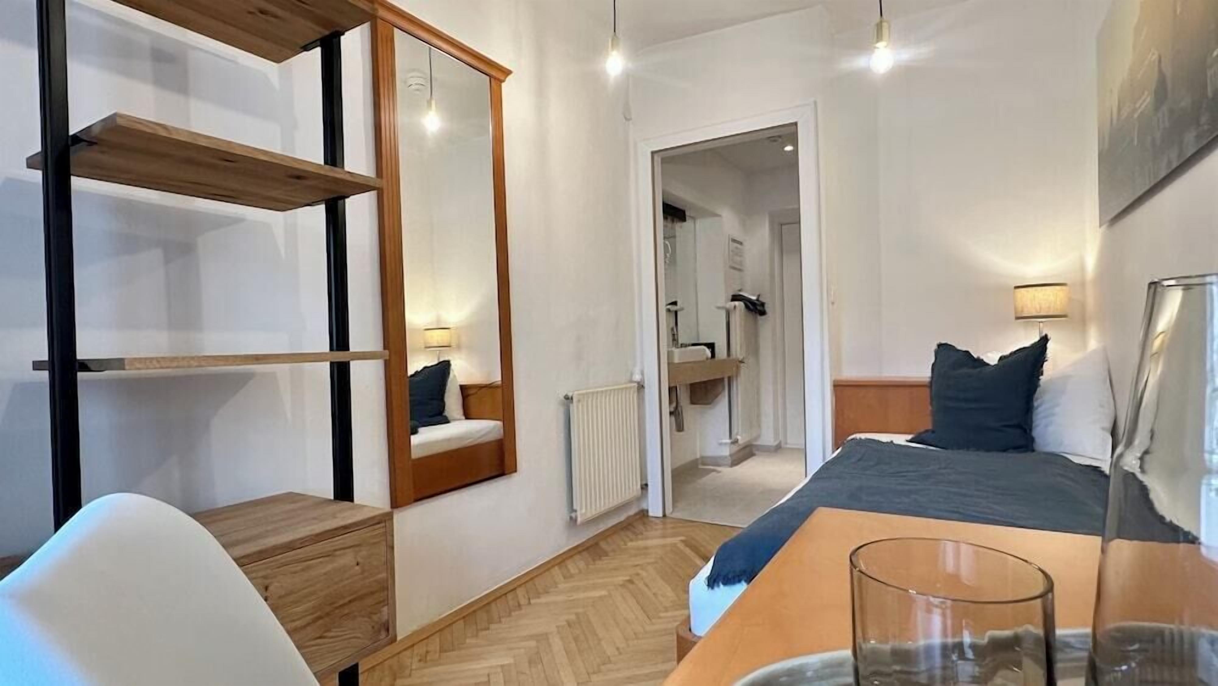 A modern hotel room with a bed, bedside table, chair, and a mirror.