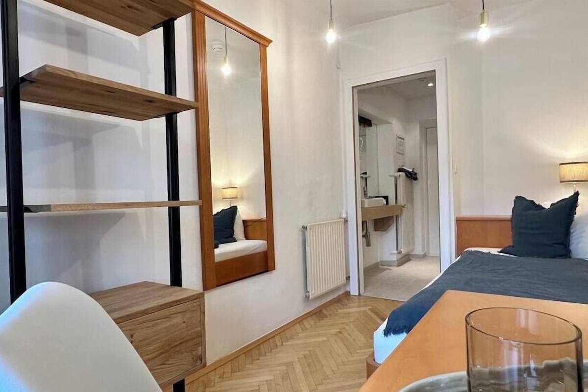A modern hotel room with a bed, bedside table, chair, and a mirror.