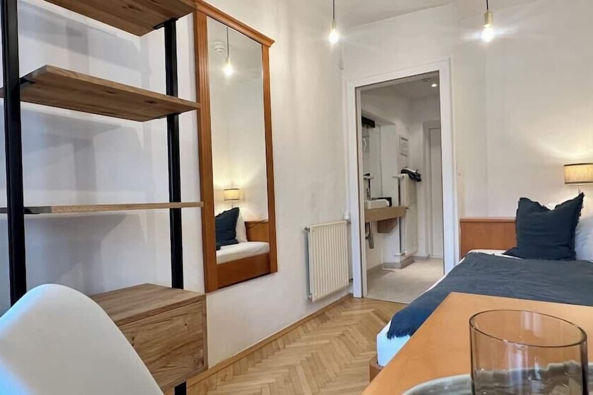 Ein modernes Hotelzimmer mit Bett, Nachttisch, Sessel und Spiegel.
