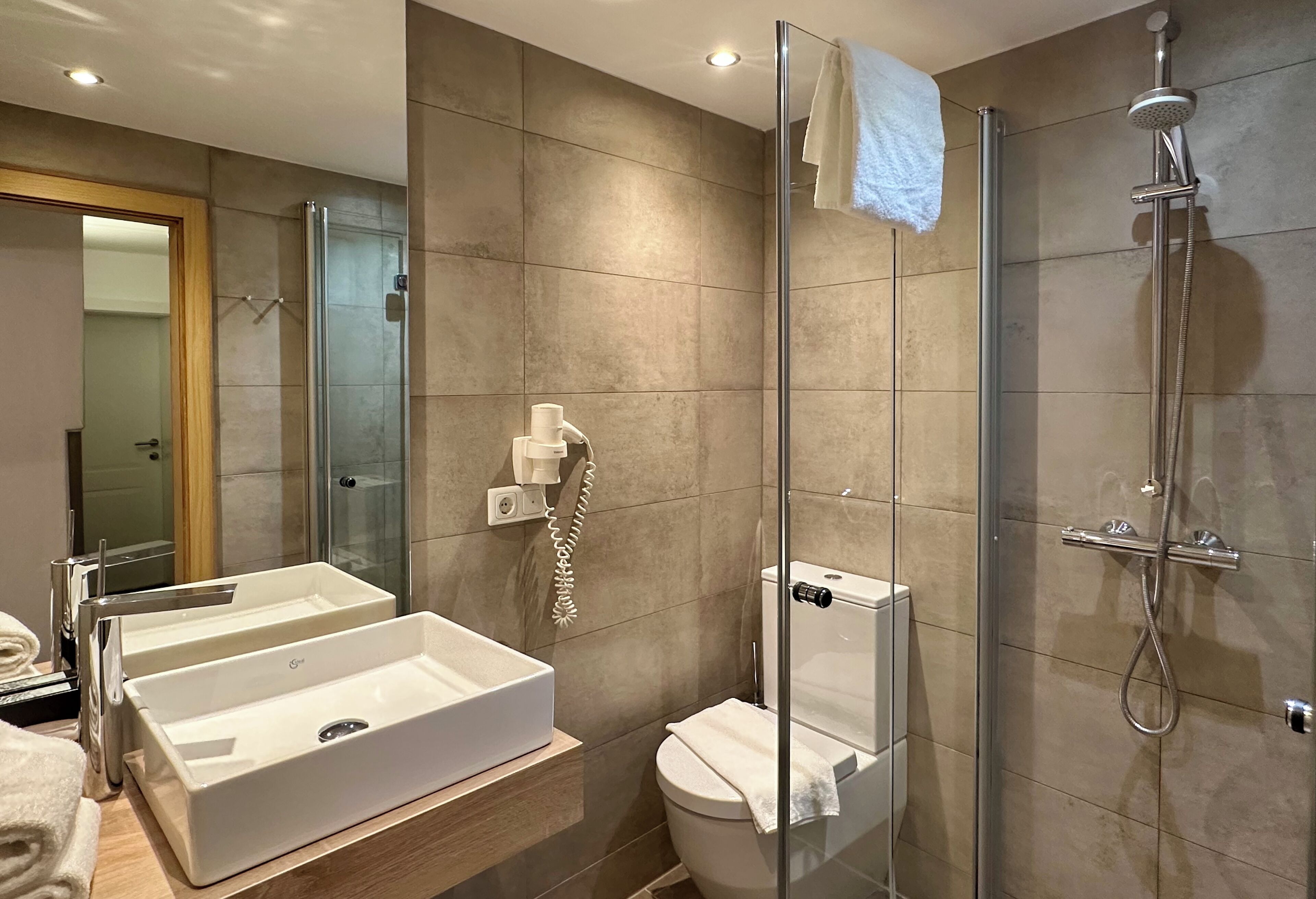 Ein modernes Badezimmer mit einer Duschkabine, zwei Waschbecken und einer Toilette.