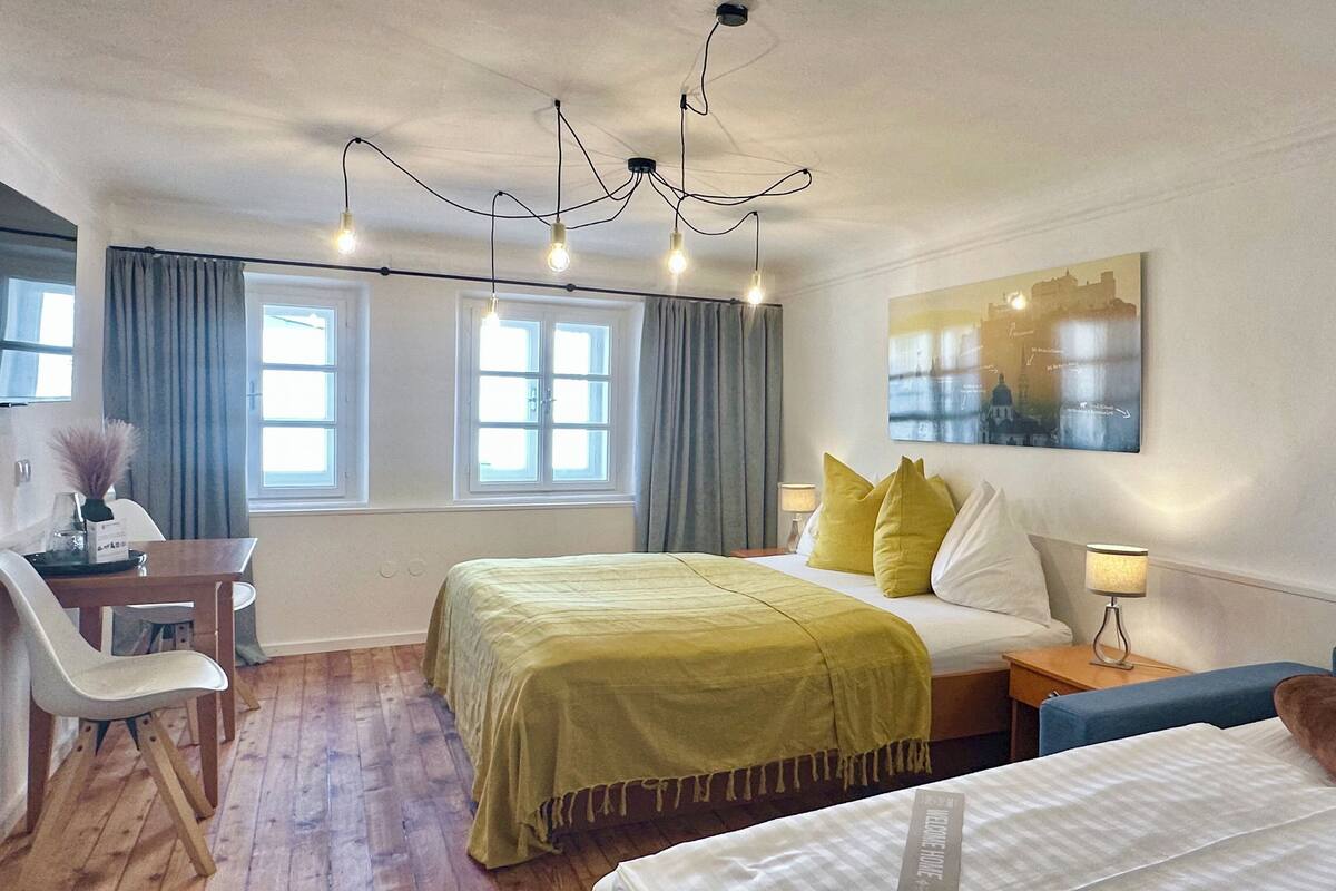 A hotel room with a bed, bedside table, lamp, chair, and a desk with a lamp.