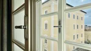 Ett fönster med en vit ram och ett dörrhandtag, som speglar en byggnad med flera fönster och en balkong.