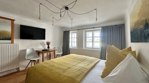 Habitación de hotel con cama, escritorio, silla, televisor y dos ventanas con cortinas.