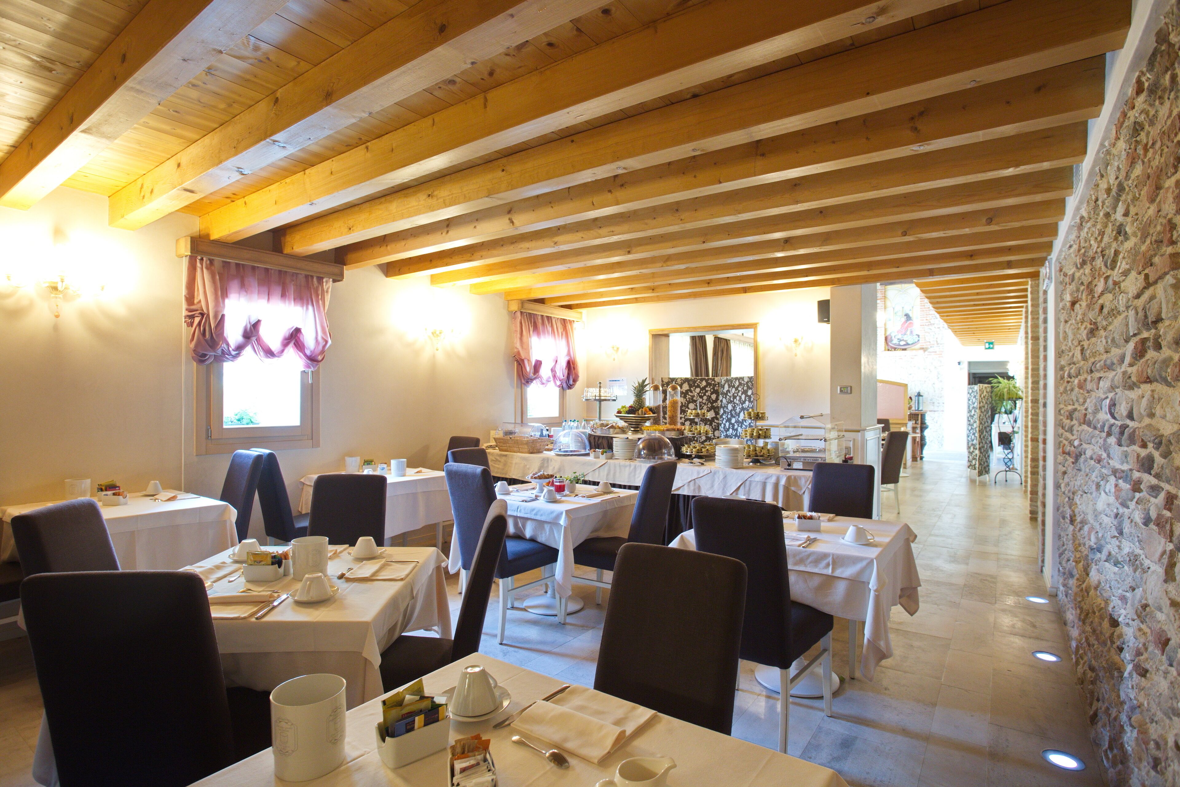 A restaurant with wooden beams, tables set with white tablecloths, and chairs.