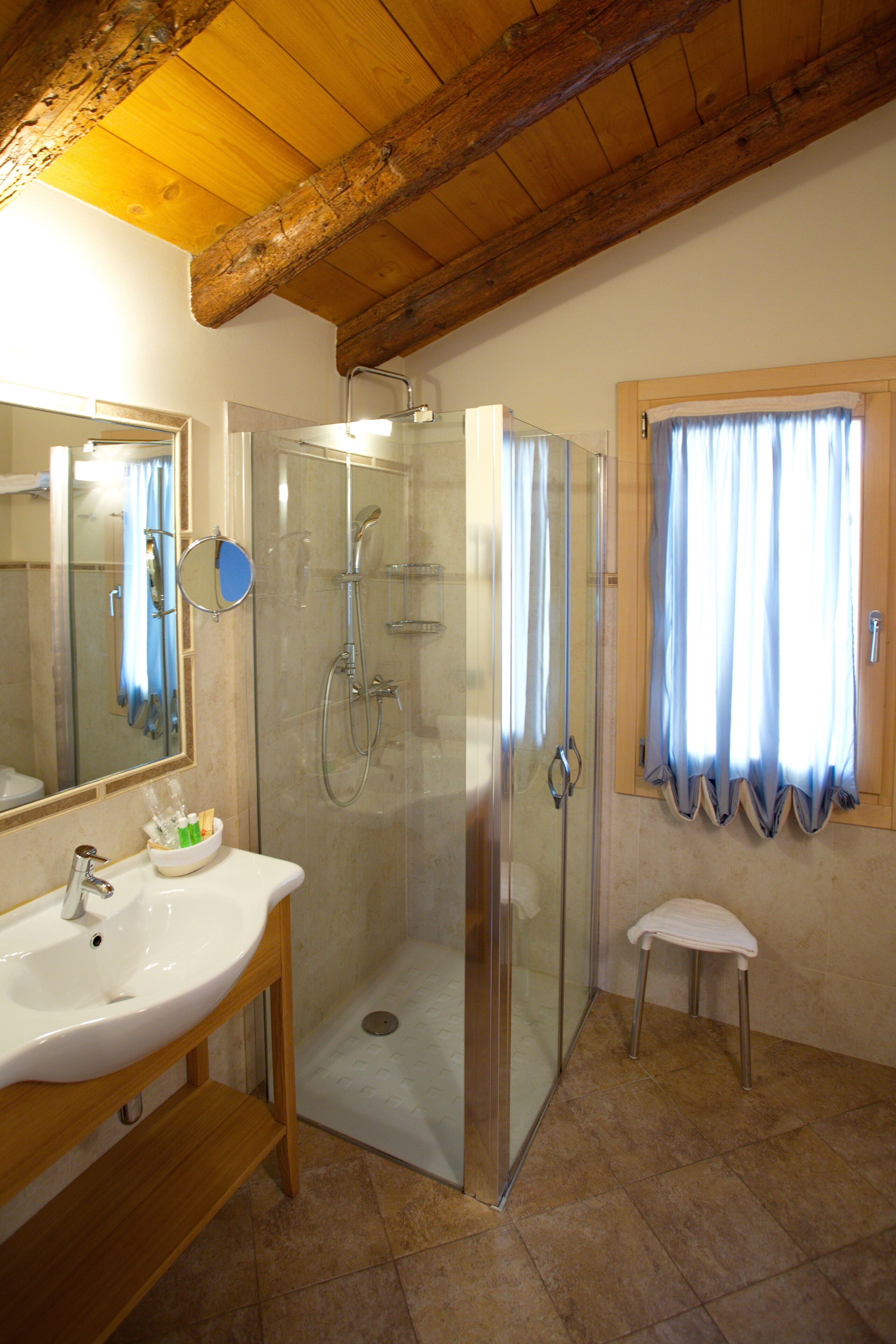 Un baño con cabina de ducha de vidrio, lavamanos con espejo y ventana con cortinas.