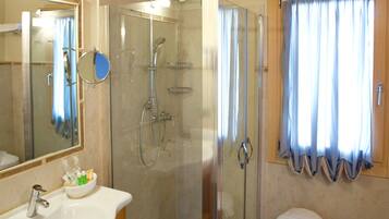 Un baño con cabina de ducha de vidrio, lavamanos con espejo y ventana con cortinas.